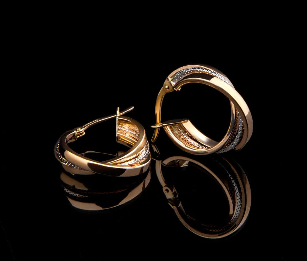 A pair of gold earrings sitting on top of a black surface.